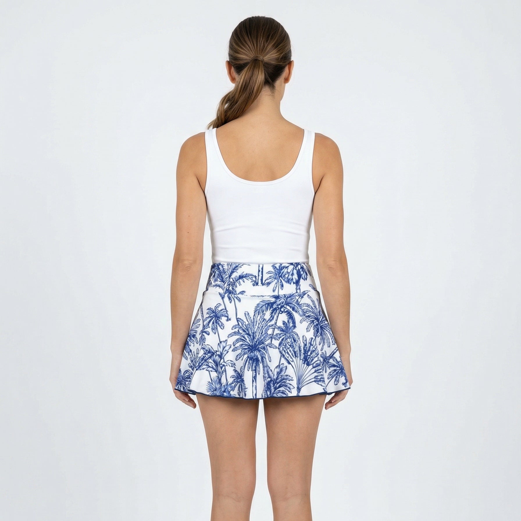 Person wearing a white tank top and blue and white patterned skirt on a white background
