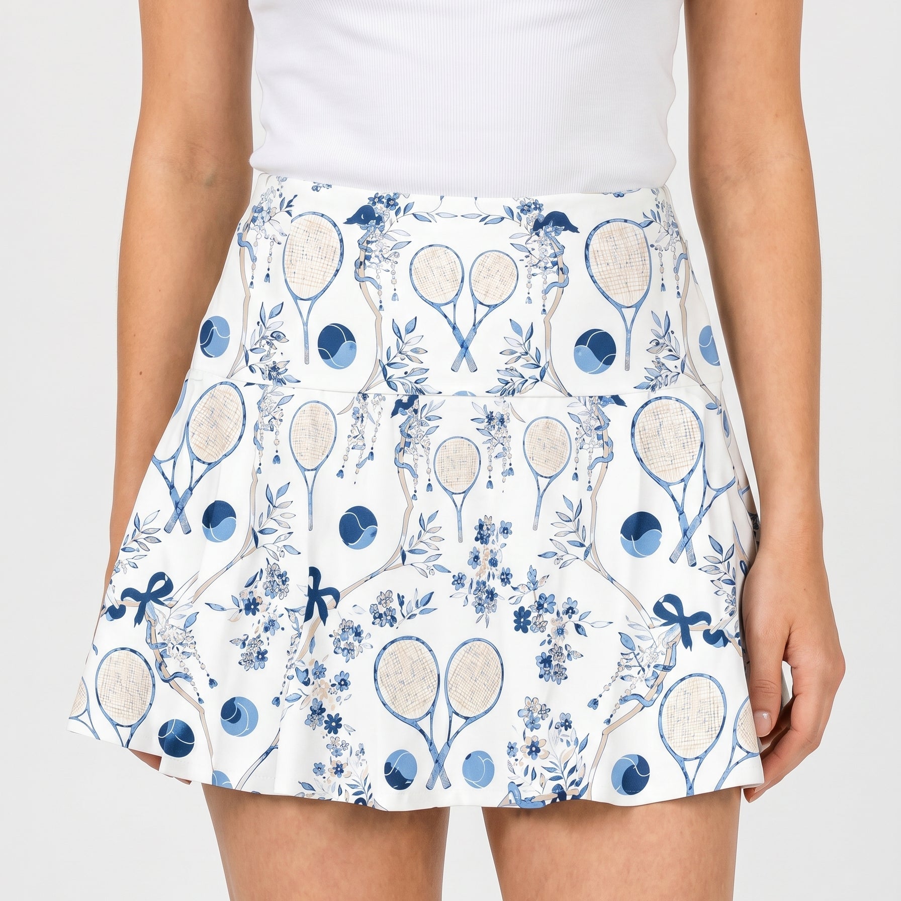 Person wearing a white tank top and a patterned skirt with tennis racket design on a plain background