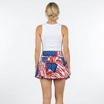Woman wearing a white tank top and American flag patterned skirt on a plain background
